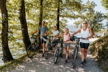Familie mit Fahrrädern genießt eine sommerliche Radtour entlang des Zeller Sees in der Natur rund um das Familienhotel Amiamo.