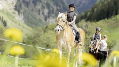 Zwei Kinder reiten im Familienhotel Oberkarteis im Salzburger Land vor Bergkulisse auf einem Weg.
