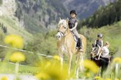 Zwei Kinder reiten im Familienhotel Oberkarteis im Salzburger Land vor Bergkulisse auf einem Weg.