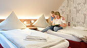 Zwei Kinder sitzen auf dem Bett und lesen ein Buch im Familienzimmer des Familienhotels Rhön Feeling.