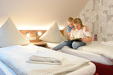 Zwei Kinder sitzen auf dem Bett und lesen ein Buch im Familienzimmer des Familienhotels Rhön Feeling.