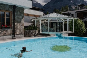 Eine Frau schwimmt im beheizten Außenpool mit Panoramablick auf die Berge im Familienhotel Tirolerhof