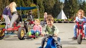 Mehrere Kinder flitzen mit Gokarts und Rutschfahrzeugen über den Hof im Familienhotel Ramsi in Kärnten