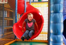 Ein lachendes Mädchen rutscht eine rote Rutsche in der Softplayanlage im Familienhotel Ramsi in Kärnten hinunter