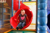 Ein lachendes Mädchen rutscht eine rote Rutsche in der Softplayanlage im Familienhotel Ramsi in Kärnten hinunter