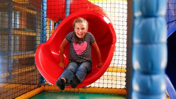 Ein lachendes Mädchen rutscht eine rote Rutsche in der Softplayanlage im Familienhotel Ramsi in Kärnten hinunter