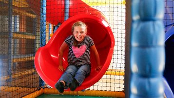 Ein lachendes Mädchen rutscht eine rote Rutsche in der Softplayanlage im Familienhotel Ramsi in Kärnten hinunter