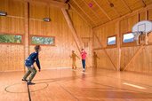 Zwei Kinder spielen Basketball in der hellen Turnhalle des Familienhotels Ramsi mit Holzverkleidung und hohen Decken