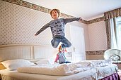 Kinder springen auf dem Bett im Familienzimmer des Familienhotels Borchard's Rookhus an der Mecklenburgischen Seenplatte.