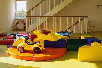 Bunter und sicherer Indoor-Spielbereich im Familienhotel Deichkrone mit weichen Schaumstoffblöcken, einem kleinen gelben Kinderfahrzeug und einem Kriechtunnel, ideal für Spiel und Spaß bei den jüngsten Gästen.