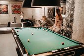 Eine Familie spielt in der Playfactory des Familienhotel Mia Alpina in Tirol Billard in einem gemütlichen Spielbereich.