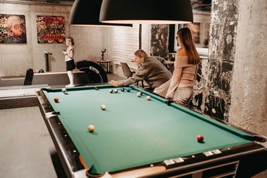 Eine Familie spielt in der Playfactory des Familienhotel Mia Alpina in Tirol Billard in einem gemütlichen Spielbereich.