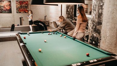 Eine Familie spielt in der Playfactory des Familienhotel Mia Alpina in Tirol Billard in einem gemütlichen Spielbereich.
