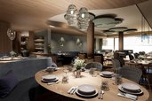 Visualisierung der neuen Stube im Familienhotel Zauchenseehof mit stilvollem Holzdesign, runden Tischen und moderner Beleuchtung.
