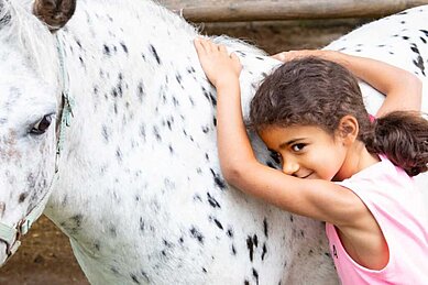Ein Kind kuschelt mit einem Pferd im Familienhotel Der Ponyhof Steiermark.