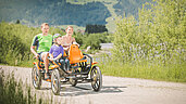 Familie in Tirol bei einem Ausflug in die Natur im Familienurlaub im Familienhotel Landgut Furtherwirt. Die Familie fährt zu dritt auf einem Vierrad den Bach entlang.