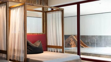 Gemütliche Ruheliegen mit Vorhängen im Wellnessbereich des Familienhotel Oberkarteis mit Blick auf den Pool.