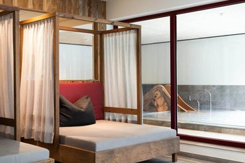 Gemütliche Ruheliegen mit Vorhängen im Wellnessbereich des Familienhotel Oberkarteis mit Blick auf den Pool.