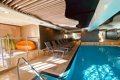 Das Indoor-Schwimmbad im Wellness- & Familienhotel Egger in Saalbach Hinterglemm ist gemütlich eingerichtet mit Pflanzen und Liegen zum Entspannen.