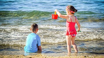 Zwei Kinder planschen am schönen Sandstrand im Familienurlaub in der Toskana.