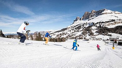 Kinder fahren die Skipiste mit einer Betreuerin in der Nähe vom Familienhotel Engel Gourmet & Spa in Südtirol runter.