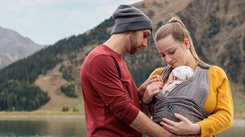 Familie mit Baby stehen vor einem See und einer Berglandschaft beim Familienhotel Kaiserhof in Tirol.