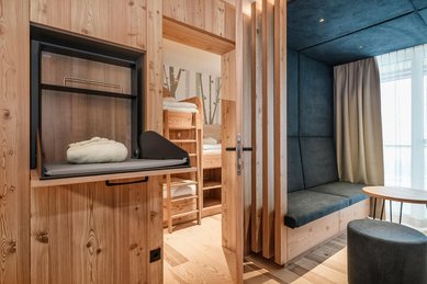 Gemütliches Familienzimmer im Familienhotel mit viel Holz, separatem Kinderbereich mit Etagenbett und Sitzecke für ein entspannten Urlaub.