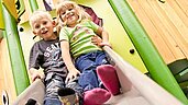 Zwei fröhliche Kinder rutschen gemeinsam auf einer bunten Indoor-Rutsche in der KinderWelt des Familienhotels Sonnenhügel.