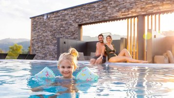 Mädchen planscht im Pool im Sommerurlaub im Familienhotel im Bayerischen Wald und die Eltern entspannen am Beckenrand