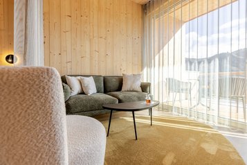 Heller Wohnbereich mit moderner Couch und Blick auf den Balkon im Familienhotel Almfamilyhotel Scherer in Osttirol.