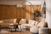 Gemütlicher Lobbybereich im Familienhotel Alpenhotel Kindl mit beigen Sofas, runder Stehlampe und Holzwandverkleidung.