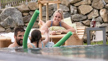 Familie planscht im Urlaub im Outdoor-Pool in einem Familotel