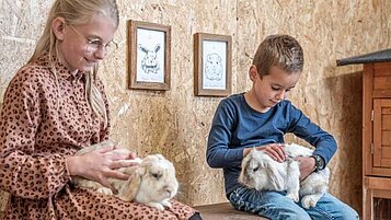 Kinder sitzen im Stall und streicheln Hasen im Familienhotel Almfamilyhotel Scherer in Tirol.