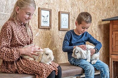 Kinder sitzen im Stall und streicheln Hasen im Familienhotel Almfamilyhotel Scherer in Tirol.
