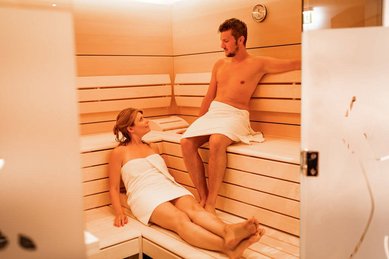 Ein Paar entspannt in der modernen Sauna des Familienhotels Amiamo und genießt die wohltuende Wärme in ruhiger Atmosphäre.