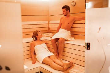 Ein Paar entspannt in der modernen Sauna des Familienhotels Amiamo und genießt die wohltuende Wärme in ruhiger Atmosphäre.
