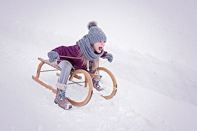 Kind rodelt mit dem Schlitten die Piste hinunter im Familienhotel Das Kaltschmid in Seefeld Tirol.