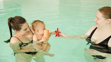Eine Mutter ist im Hotel-Pool und hält ihr Baby im Arm. 