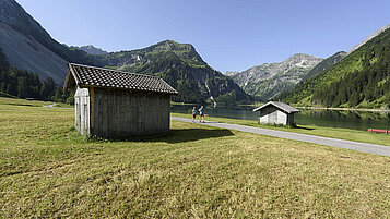 Eine atemberaubende Landschaft erstreckt sich in Tirol. Zwei Hütten zieren den Wegrand während zwei Wanderer sie passieren.