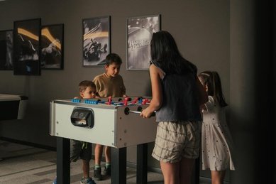 Kinder spielen lachend Tisch-Kicker mit gleichaltrigen in ihrem Urlaub im Familienhotel Engel Gourmet & Spa in Südtirol