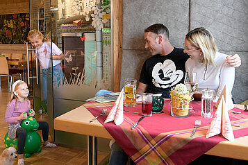 Mutter und Vater beim Essen im Restaurant des Familienhotels Rhön Feeling während die beiden Kinder nebenan im Spielbereich spielen.