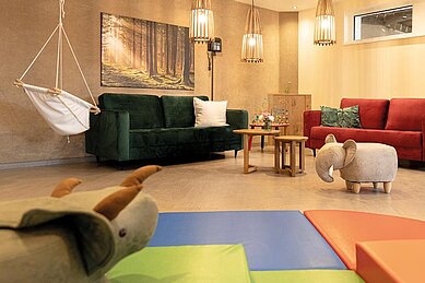 Liebevoll eingerichteter Spielraum für Kinder mit zwei bunten Sofas und Schaukel im Familienhotel Sonnenpark.