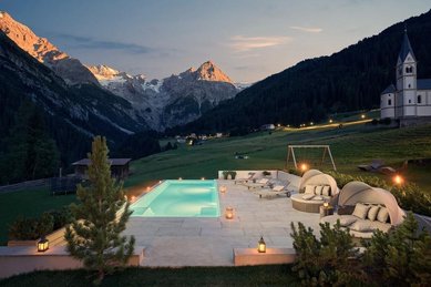 Der Außenpool im Familienhotel Bella Vista in Südtirol leuchtet am Abend mit Liegen, Sonnenschirmen und Bergkulisse.
