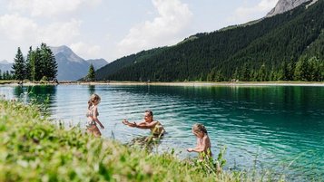 Eine Familien geht in einem Bergsee schwimmen.