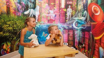 Zwei Kinder sitzen an einem Tisch vor einer farbenfrohen Wand in der Magischen Abenteuerwelt des Familienhotels Kaiserhof in Tirol, aufgenommen im Bereich Magische Bibliothek.