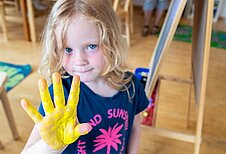 Kleines Mädchen mit ausgestreckter, gelb bemalter Handfläche im Happy-Club des Familienhotels Alpengasthof Hochegger.