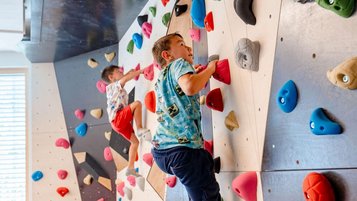 Zwei Jungs im Teenager-Alter klettern an der bunten Boulderwand im Familienhotel Amiamo in Zell am See.