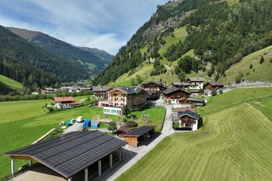 Luftaufnahme des Familienhotels Oberkarteis inmitten grüner Wiesen und Berge mit modernem Stallgebäude und Spielbereich für Kinder.