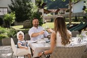 Familie genießt ein entspanntes Mittagessen auf der Terrasse des Familienhotels Alpenhotel Kindl bei Sonnenschein.