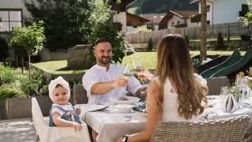 Familie genießt ein entspanntes Mittagessen auf der Terrasse des Familienhotels Alpenhotel Kindl bei Sonnenschein.